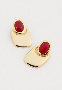 Kultakappaleiset korvakorut, joissa on kiiltävä pinta ja abstraktissa muotoilussa olevat ovaalit punaiset kivet. Sujuva, kiillotettu pinta ja kaarevat muodot.