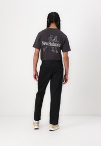 Gray cotton t-shirt featuring a white printed design of two runners and "New Balance" text. Worn with black trousers and beige sneakers.
