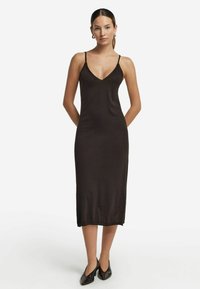 Svart midi-klänning med ärmlös V-ringning. Tillverkad av mjukt tyg, har den tunna axelband och en rak skärning som når till mitten av vaden.