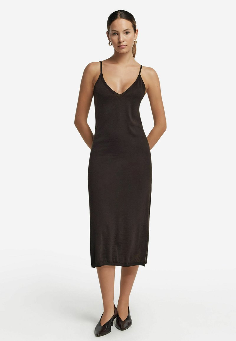 Svart midi-klänning med ärmlös V-ringning. Tillverkad av mjukt tyg, har den tunna axelband och en rak skärning som når till mitten av vaden.