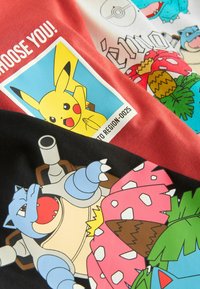 Tre t-shirts i rød, hvid og sort med farverige Pokémon grafiktryk. Fremtrædende karakterer inkluderer Pikachu, Blastoise og Bulbasaur.