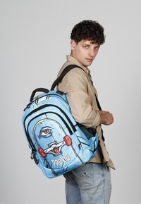 Mochila azul con un diseño gráfico de un ojo y acentos rojos. Hecha de material duradero, con correas negras ajustables y un bolsillo con cremallera.