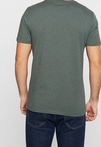 Dunkelgrünes T-Shirt aus leichtem Baumwollstoff, mit Rundhalsausschnitt und kurzen Ärmeln, kombiniert mit dunkelblauen Jeans.