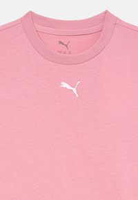 Rožinė crew neck marškinėliai su baltu Puma logotipu centre, žemiau apykaklės.
