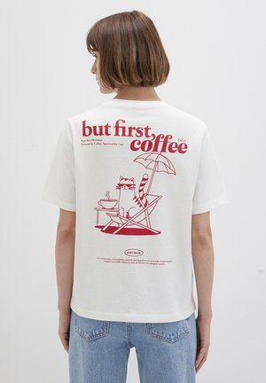 Weißes Baumwoll-T-Shirt mit einem roten Grafikdruck auf dem Rücken, der eine Katze zeigt, die in einem Stuhl unter einem Schirm entspannt, begleitet von kaffeebezogenen Text.
