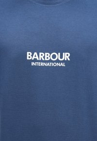 Μπλε βαμβακερό t-shirt με αντίθετο λευκό λογότυπο που γράφει "BARBOUR INTERNATIONAL" με έντονα, κεφαλαία γράμματα.