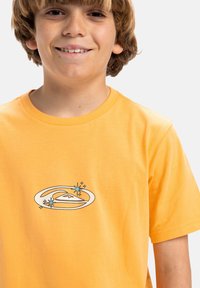 Camiseta de algodón naranja con un gráfico circular que presenta una ola y acentos de estrellas en azul y blanco. Diseño de mangas cortas y cuello redondo.