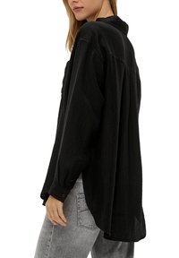 Zwarte button-up shirt van een textuurstof, met een losse pasvorm en een hoge-lage zoomlijn. Beschikt over omgekrulde lange mouwen en een kraag.