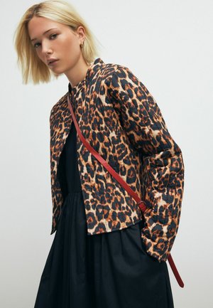 Leopard-print quilted jacket in shades of orange and black, with a sleek design and a red shoulder strap. Worn over a black dress.