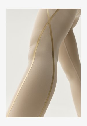 Beiga leggings med en slät textur och gyllene accentlinjer som skapar ett X-mönster längs sidan. Närbild på tyget.