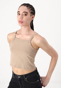 Svetlohnedý crop top s tenkými ramienkami, tvarovaným výstrihom a hladkou textúrou, kombinovaný s čiernymi nohavicami s vysokým pásom.