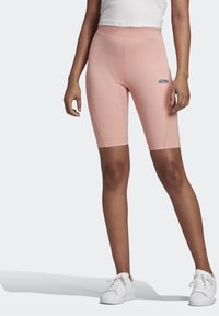 Ljusrosa cykelshorts med hög midja, slät textur och logotypapplikation. Bärs med vita sneakers för kontrast.