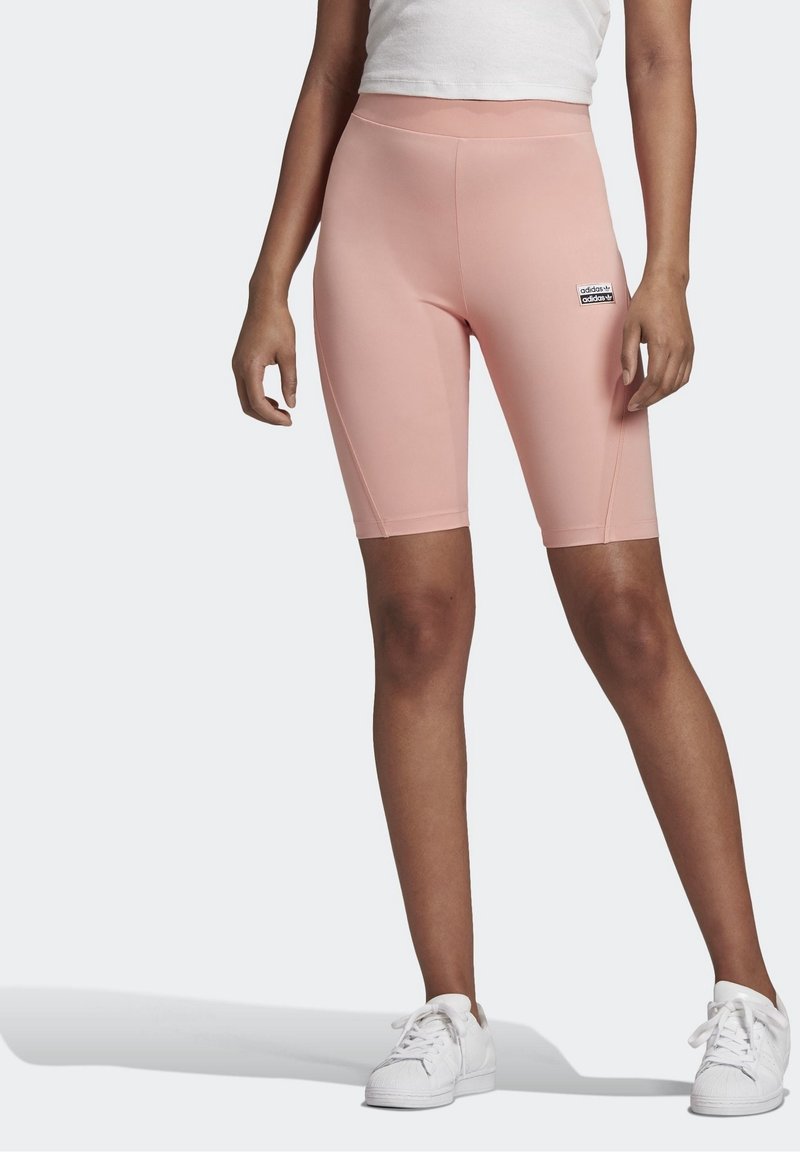 Ljusrosa cykelshorts med hög midja, slät textur och logotypapplikation. Bärs med vita sneakers för kontrast.