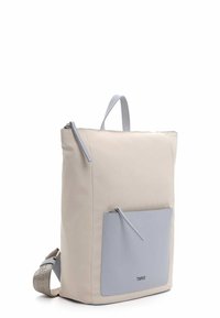 Mochila de tela beige con un bolsillo frontal de cuero gris, cierre de cremallera y una correa de hombro desmontable. Cuenta con un asa superior para llevarla.