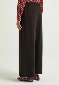 Pantaloni neri a gamba larga con una texture liscia e vita elasticizzata, abbinati a una maglia rossa con motivo e scarpe multicolori.