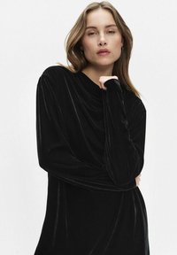 Schwarzsamtes Kleid mit langen Ärmeln, das über einen drapierten Ausschnitt und eine fließende Silhouette verfügt, mit glatter Textur und weit geschnittenen Ärmeln.