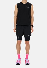 Top negro sin mangas, pantalones cortos a juego y mallas de compresión negras. Cuenta con calcetas rosa brillante y zapatillas deportivas multicolores con una suela texturizada.