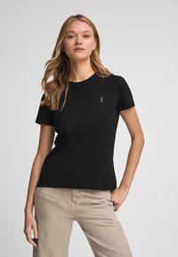 Svart kortärmad t-shirt i mjuk bomullsblandning, med en minimalistisk broderad design på bröstet. Klassisk rund hals och figurnära passform.