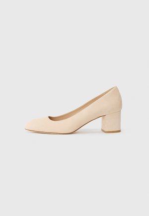Zapatos de tacón medio para mujer en ante beige con punta redondeada y tacón cuadrado sobre un fondo blanco liso.