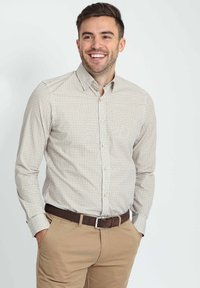 Lange mouwen knoopshirt in lichtbeige met een geometrisch patroon; heeft een kraag en wordt gecombineerd met kaki broeken en een leren bruine riem.