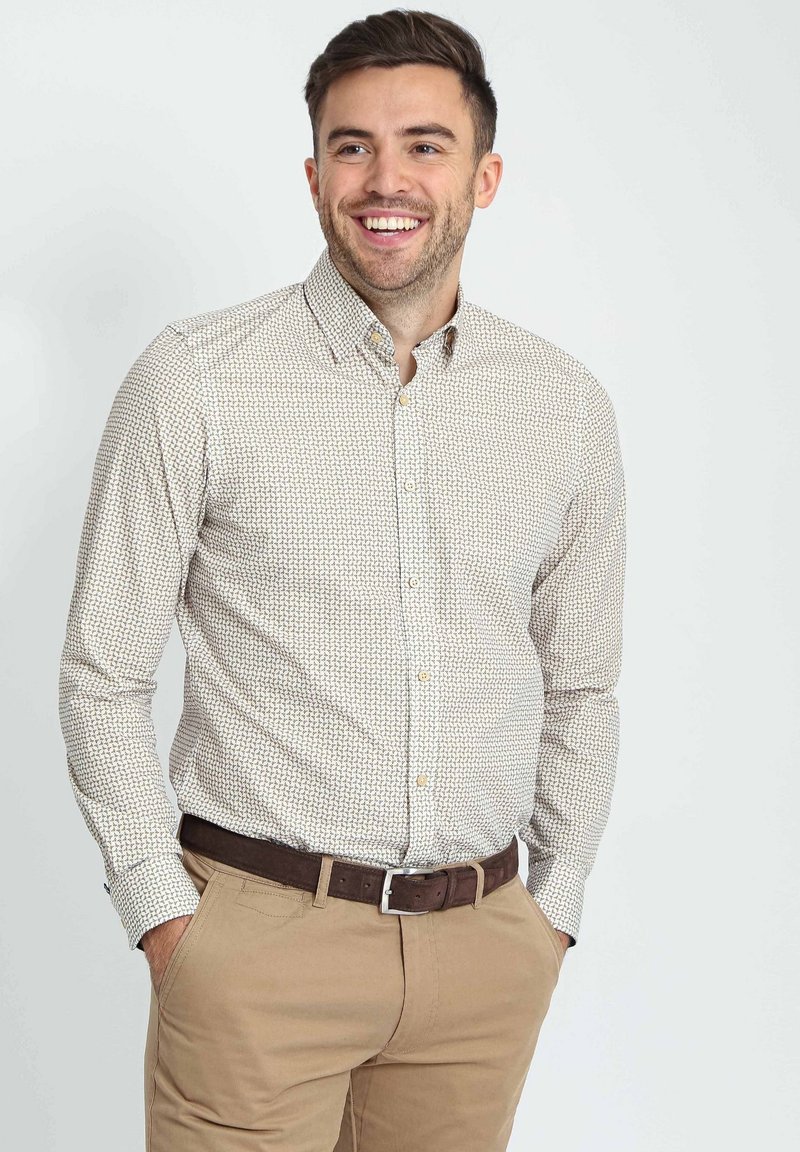 Lange mouwen knoopshirt in lichtbeige met een geometrisch patroon; heeft een kraag en wordt gecombineerd met kaki broeken en een leren bruine riem.