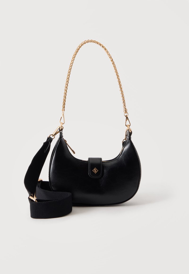 Sac à main en cuir noir en forme de croissant avec anse chaîne dorée et large bandoulière amovible en tissu noir sur fond blanc.