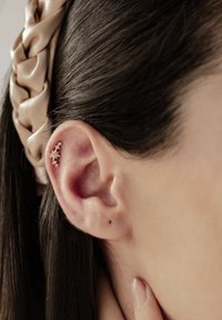 Boucle d'oreille en forme d'étoile dorée ornée de plusieurs petites pierres précieuses blanches, sur fond d'un gros plan d'une oreille humaine et de cheveux noirs lisses.