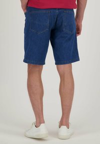 Donkerblauwe denimshorts met een klassieke snit, voorzien van twee achterzakken en een opgerolde zoom. Gecombineerd met witte schoenen. Geen zichtbare merknaam.