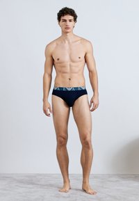 Cuecas masculinas azul-marinho com cintura elástica decorada com letras azul-claro. O tecido parece macio com uma textura suave.