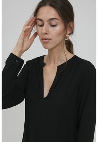 Svart långärmad blus med V-ringning, med plisserade detaljer på ärmarna och en mjuk, flödande tygtextur.