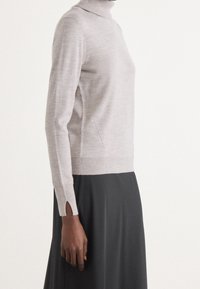 Jasnoszary sweter z golfem wykonany z miękkiego materiału. Charakteryzuje się dopasowanym krojem, długimi rękawami z bocznymi rozcięciami oraz przeszyciem po boku.