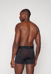 Svarta boxerkalsonger i elastiskt material, med en enhetlig färg, en svart midjeresår med logotyp och en mjuk textur.