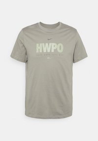 Camiseta de algodón gris con cuello redondo, que presenta un texto audaz "HWPO" y "HARD WORK PAYS OFF" en colores contrastantes y un logo de swoosh de Nike.