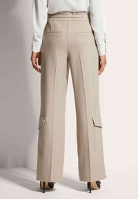 Beige broek met wijde pijpen en hoge tailleband, twee achterzakken en zijcargo zakken. Soepele stof en gepaste plooien voor extra structuur.