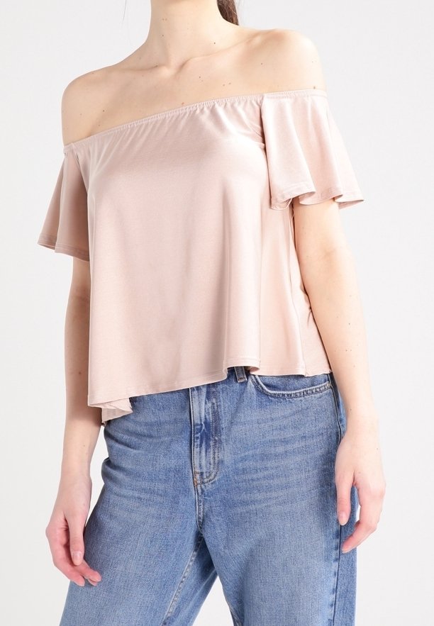 Haut rose pâle à épaules dénudées avec des manches courtes et volantées ; fabriqué en tissu lisse ; coupe ample ; associé à un jean bleu taille haute.