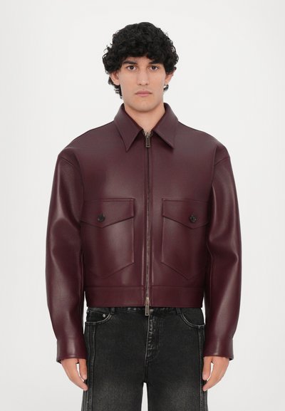 Burgundy faux leather jacket with a short cut, two chest pockets, zip-front closure, and wide collar. Smooth texture, minimal design.