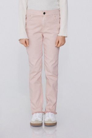 Kind trägt hellrosa Hose mit ausgefransten Säumen, ein weißes Langarmshirt mit Rüschenärmeln und weiße Turnschuhe mit beigefarbenen Akzenten.