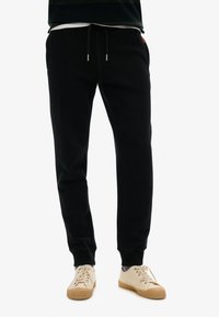 Zwarte katoenen joggers met een elastische tailleband met trekkoord, zijzakken en geribbelde boorden. Gecombineerd met beige sneakers.