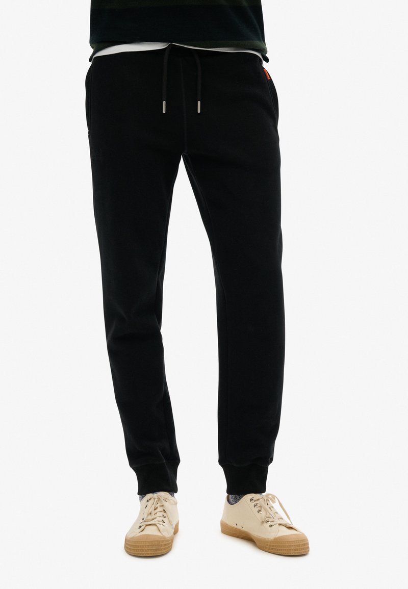 Zwarte katoenen joggers met een elastische tailleband met trekkoord, zijzakken en geribbelde boorden. Gecombineerd met beige sneakers.