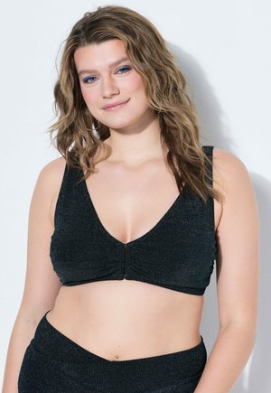 Donna sorridente con capelli mossi fino alle spalle che indossa un crop top nero testurizzato senza maniche e pantaloni abbinati a vita alta.