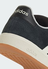 Baskets en suède noir avec une semelle blanche texturée et une semelle extérieure en caoutchouc caramel. Présente un tirant au talon en cuir noir avec le logo "adidas" en blanc.