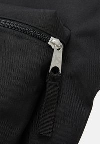 Pochette en tissu noir avec une surface texturée, dotée d'un tirette de fermeture éclair en argent gravée des initiales et d'une sangle en nylon noir pour une manipulation facile.