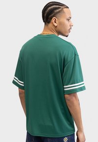 Grønn kortermet jersey med teksturert stoff. Har hvite stripede detaljer på ermene, avslappet passform og rund hals.