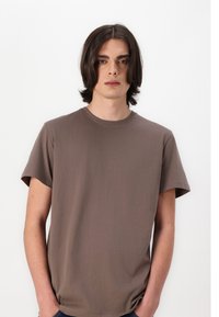 Tricou din bumbac maro, cu guler rotund, mâneci scurte și o croială relaxată. Textură netedă, design minimalist, fără modele sau accente vizibile.
