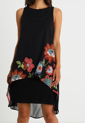 Robe noire sans manches avec ourlet asymétrique et motifs floraux colorés le long du bas à l'avant et sur les côtés.
