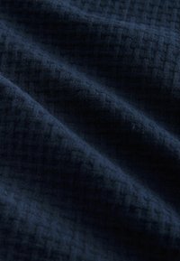 Tissu bleu foncé avec un motif en relief de petits carrés en nid d'abeille, présenté en plis doux.