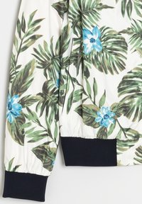 Floral bomberjack met een witte achtergrond met groene bladeren en blauwe bloemen. Inclusief elastische manchetten en een licht gewatteerd oppervlak.