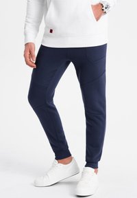 Marineblauwe joggerbroek van een zachte katoenmix, met unieke naden en twee zijzakken, gecombineerd met witte sneakers.