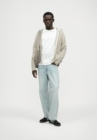 Ανοιχτό γκρι ριγέ φούτερ με μπροστινό φερμουάρ, λευκή μπλούζα από κάτω, ανοιχτό μπλε παντελόνι με ίσια γραμμή και μαύρα sneakers. Απλός σχεδιασμός.