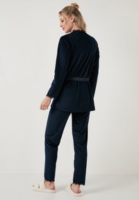 Tengerés loungewear szett puha anyagból; hosszú ujjú felső csipkés díszítéssel és hozzá illő nadrág; tartalmaz egy megkötős övet a megfelelő illeszkedéshez.